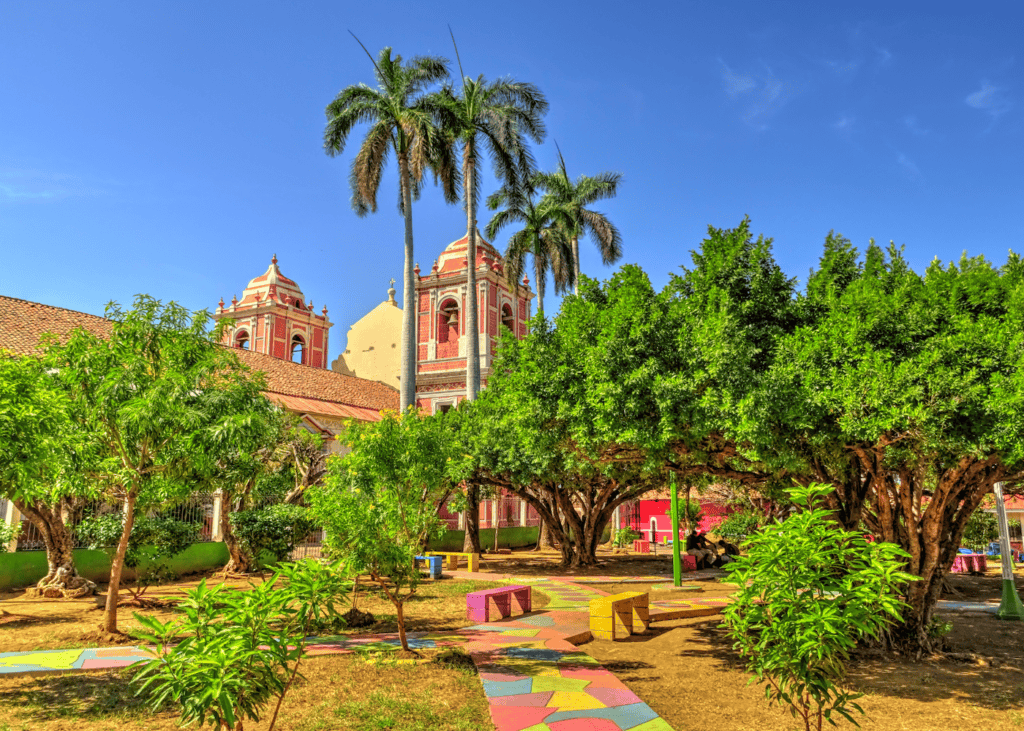 Colorful colonial plaza in León Nicaragua with a terracotta church, tall palms, and painted walkways under a bright blue sky