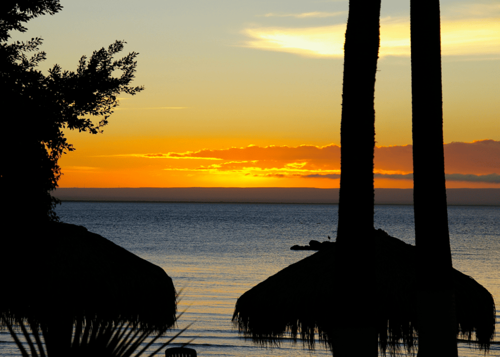 Fiery orange sunset over the Sea of Cortez in Loreto Baja Mexico with palm tree silhouettes and a palapa in the foreground