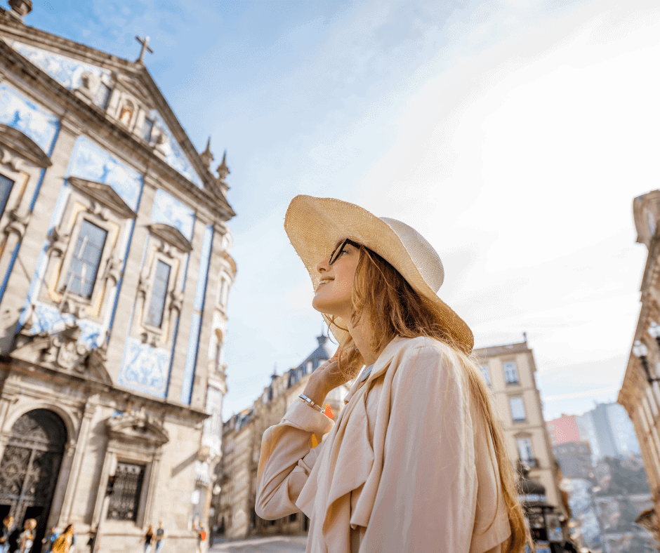 Solo female traveler in a sunhat exploring the historic streets of Porto, Portugal, beside the blue tiled Church of Santo Ildefonso.