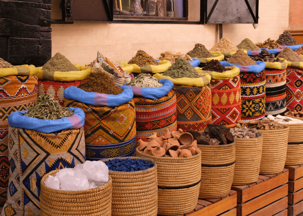Colorful woven baskets and embroidered sacks filled with mounded spices and herbs at a traditional spice souk in Marrakech, Morocco.