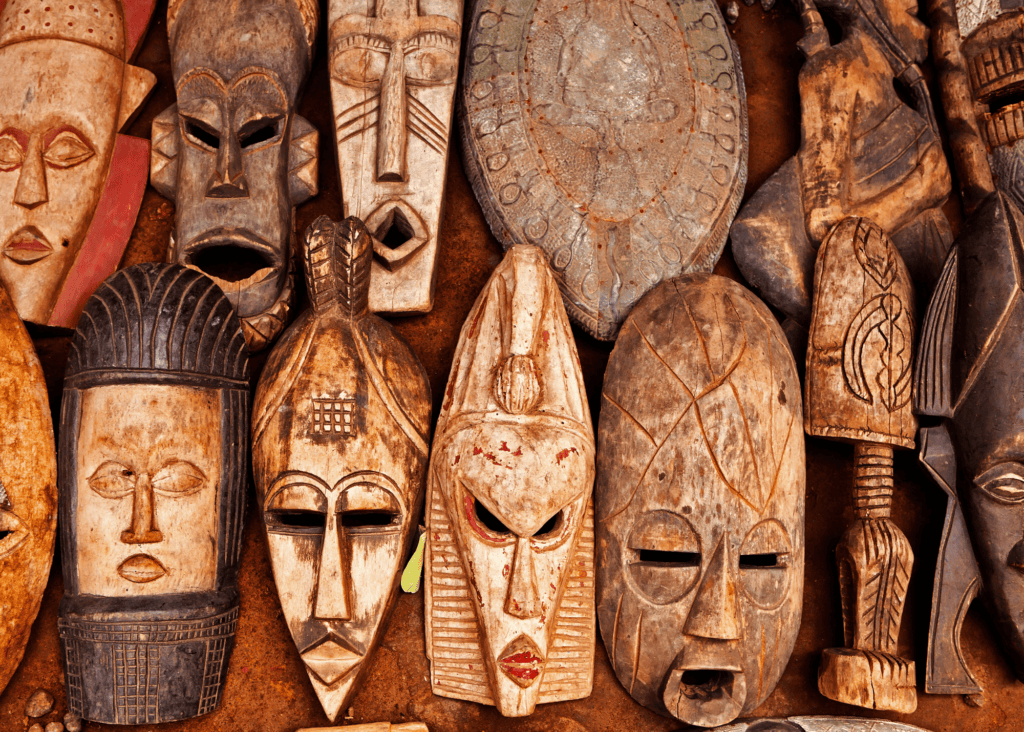Collection of handcarved traditional African wooden masks displayed together, featuring intricate geometric patterns and expressive faces representing West African cultural artistry.