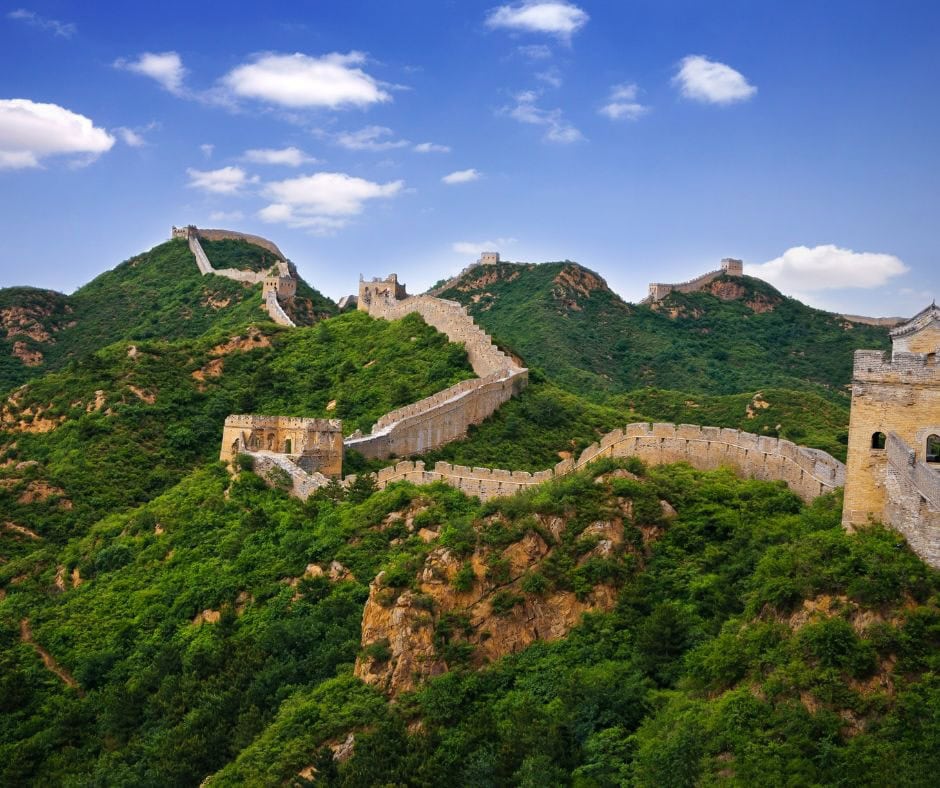 Great Wall of China winding across green mountain ridges under a blue sky.