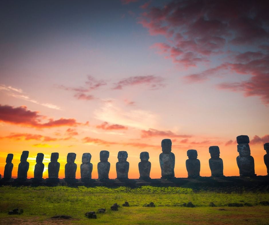 Row of Moai statues silhouetted against a colorful sunset on Easter Island, Chile.