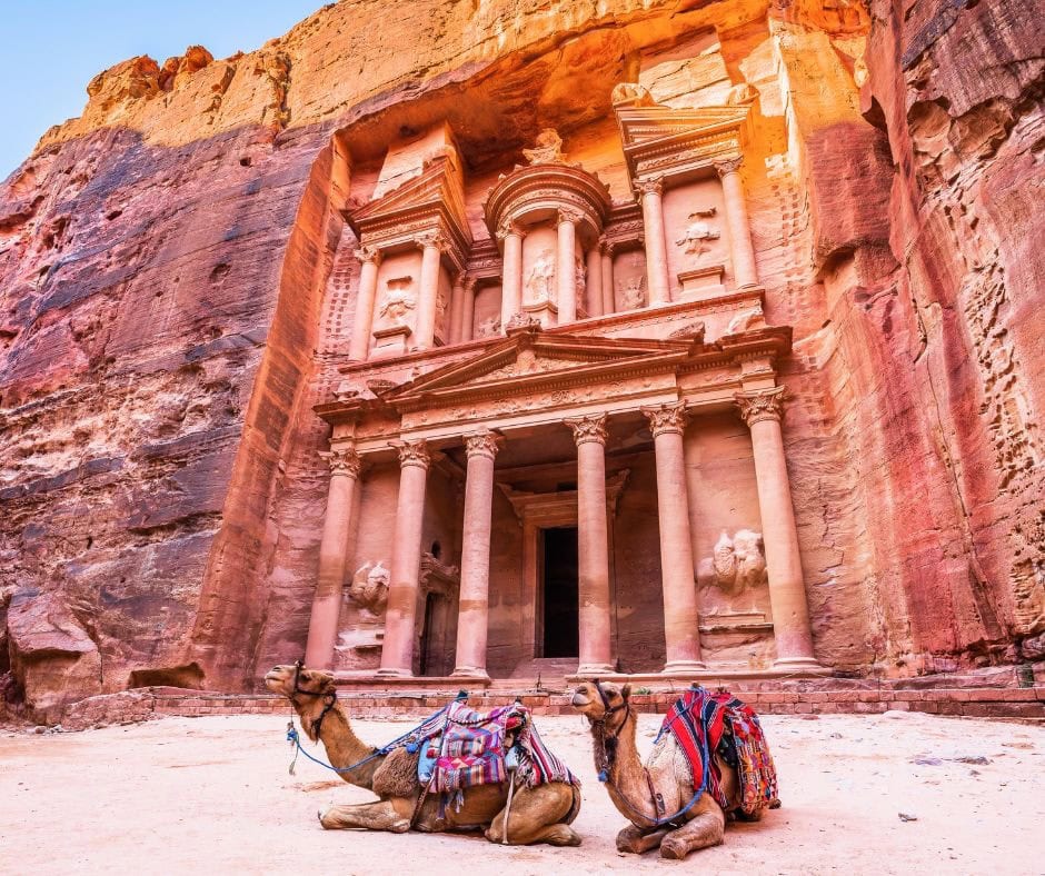 Camels resting in front of the Treasury carved into the sandstone cliffs of Petra, Jordan.