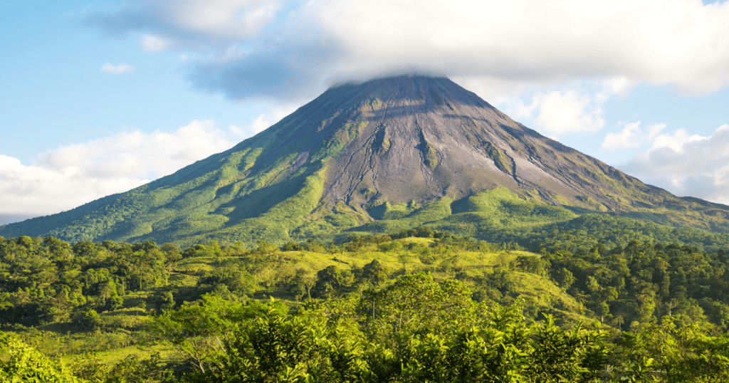 Arenal Volcano rising above lush green rainforest under a partly cloudy sky in Costa Rica.