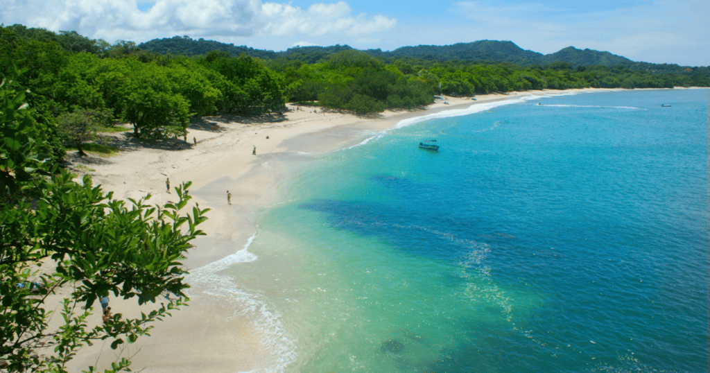 Aerial view of a white sand beach with turquoise water and lush green hills along the Pacific coast of Costa Rica.