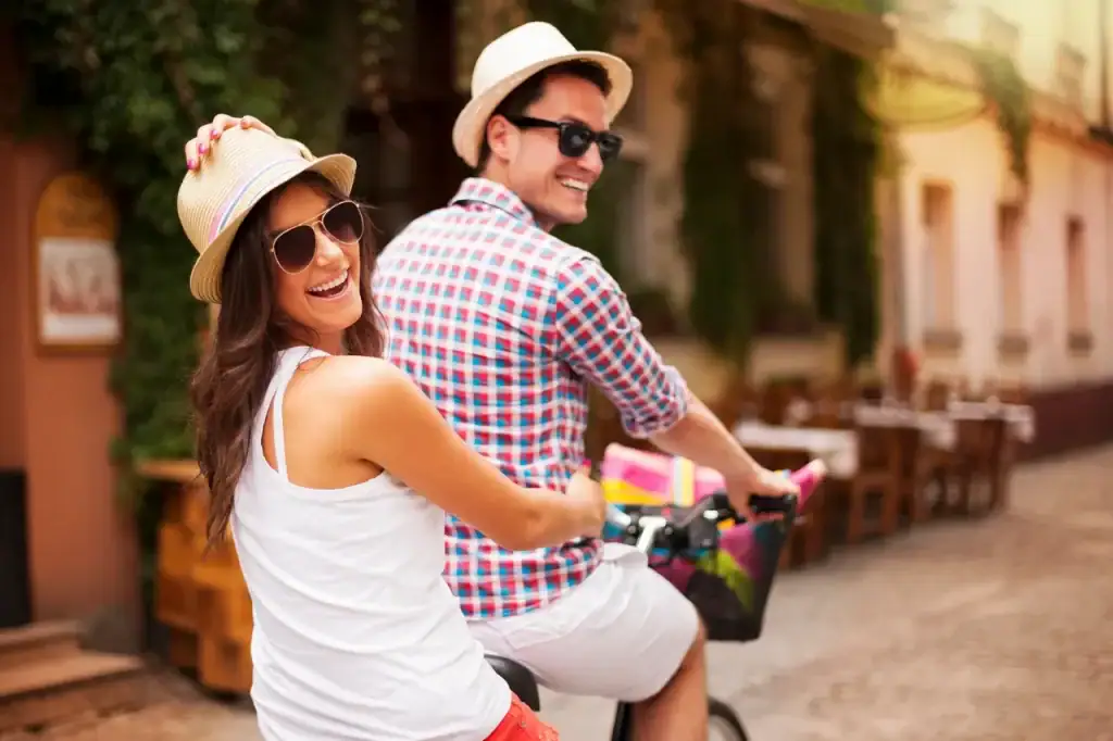 Smiling couple riding bicycles together while exploring a city on a romantic getaway.