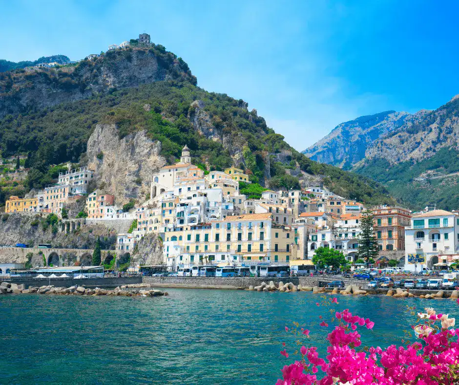 Pastel-colored buildings stacked along dramatic cliffs above the Amalfi Coast with Positano in the distance
