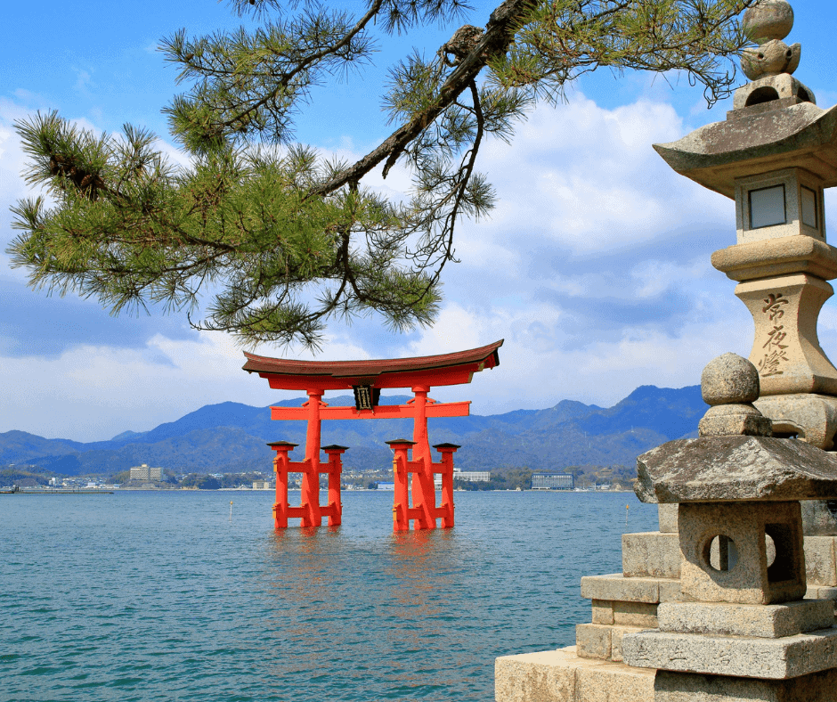 The iconic floating torii gate of Itsukushima Shrine in Miyajima, Japan, standing in the bay with a traditional stone lantern and mountain scenery in the background.