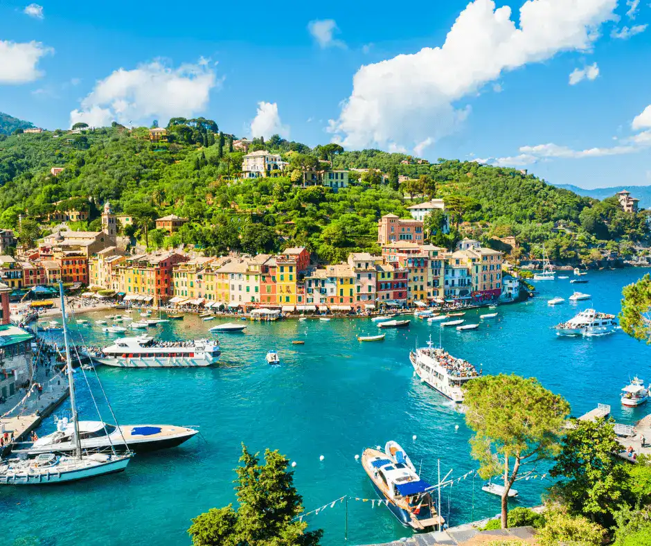 Portofino harbor with anchored sailboats, colorful waterfront buildings, and palm-lined promenade at golden hour