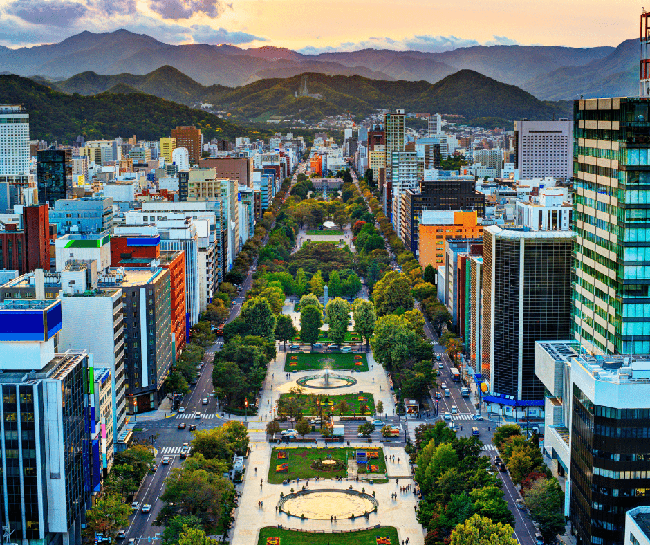 Aerial view of Sapporo, Japan, featuring Odori Park stretching through the city with mountain scenery in the background.