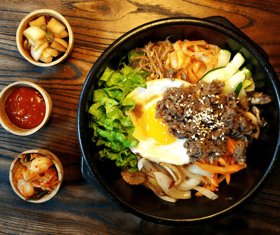Traditional Korean bibimbap topped with beef, vegetables, and a fried egg, served with kimchi and side dishes.