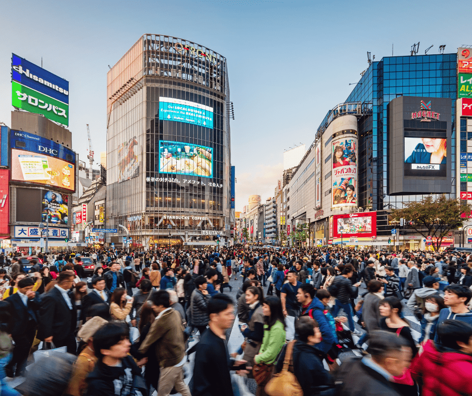 Shibuya scramble crossing in Tokyo Japan packed with crowds of pedestrians surrounded by large neon billboards and city buildings