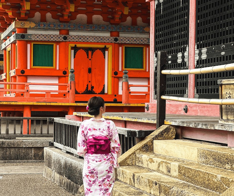 Woman in a floral kimono standing at the entrance of a colorful red temple shrine in Kyoto Japan