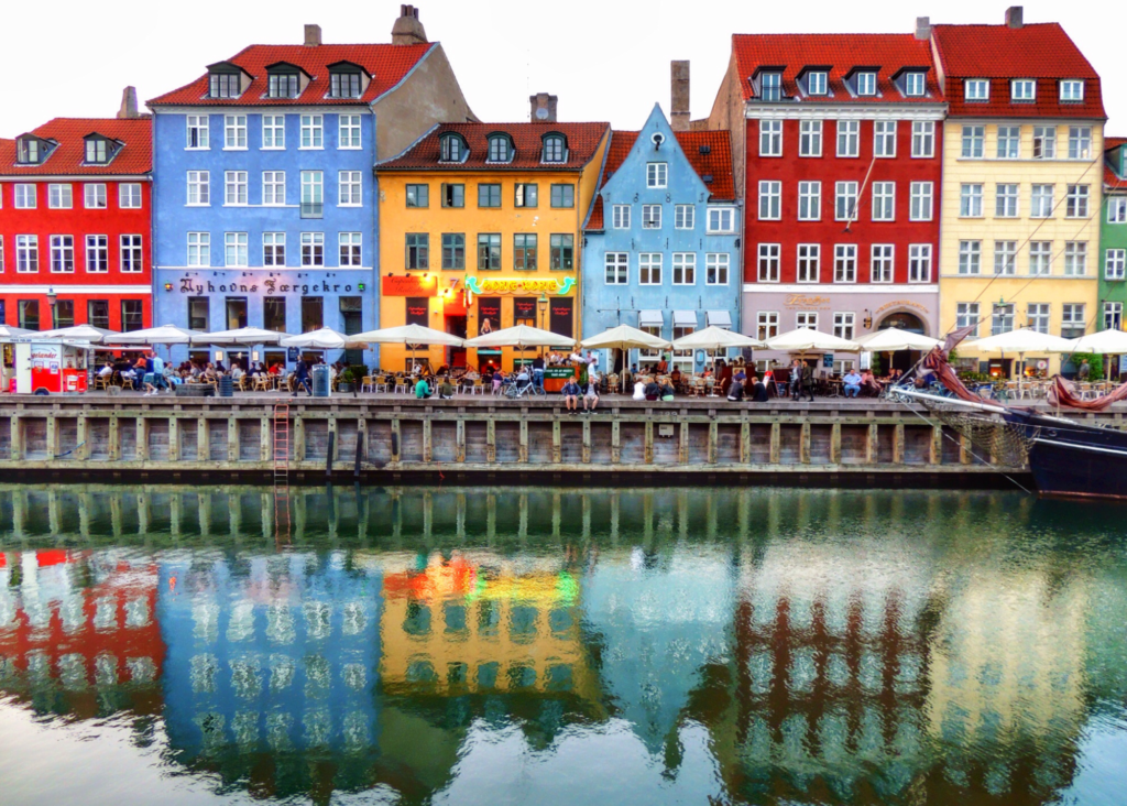 Colorful historic buildings lining the Nyhavn canal waterfront in Copenhagen Denmark with outdoor cafes and their reflections in the water.