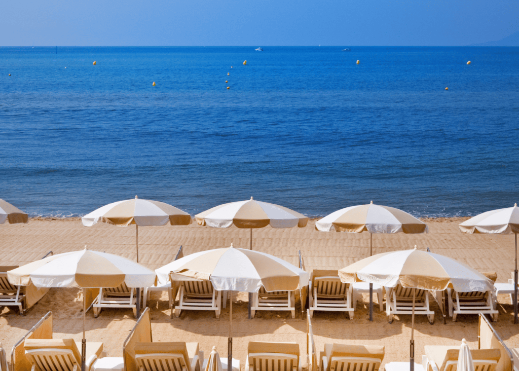 Private beach club on the French Riviera with white umbrellas and lounge chairs on the sand overlooking the blue Mediterranean sea