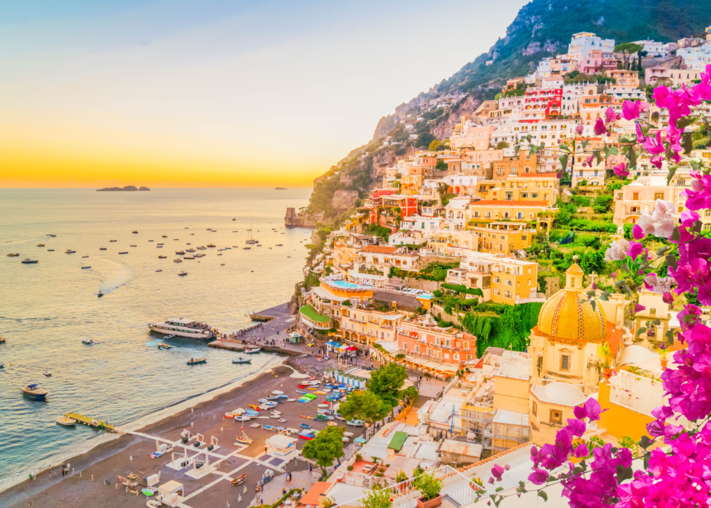 Positano village on the Amalfi Coast Italy at sunset with colorful cliffside buildings, pink bougainvillea and boats in the harbor