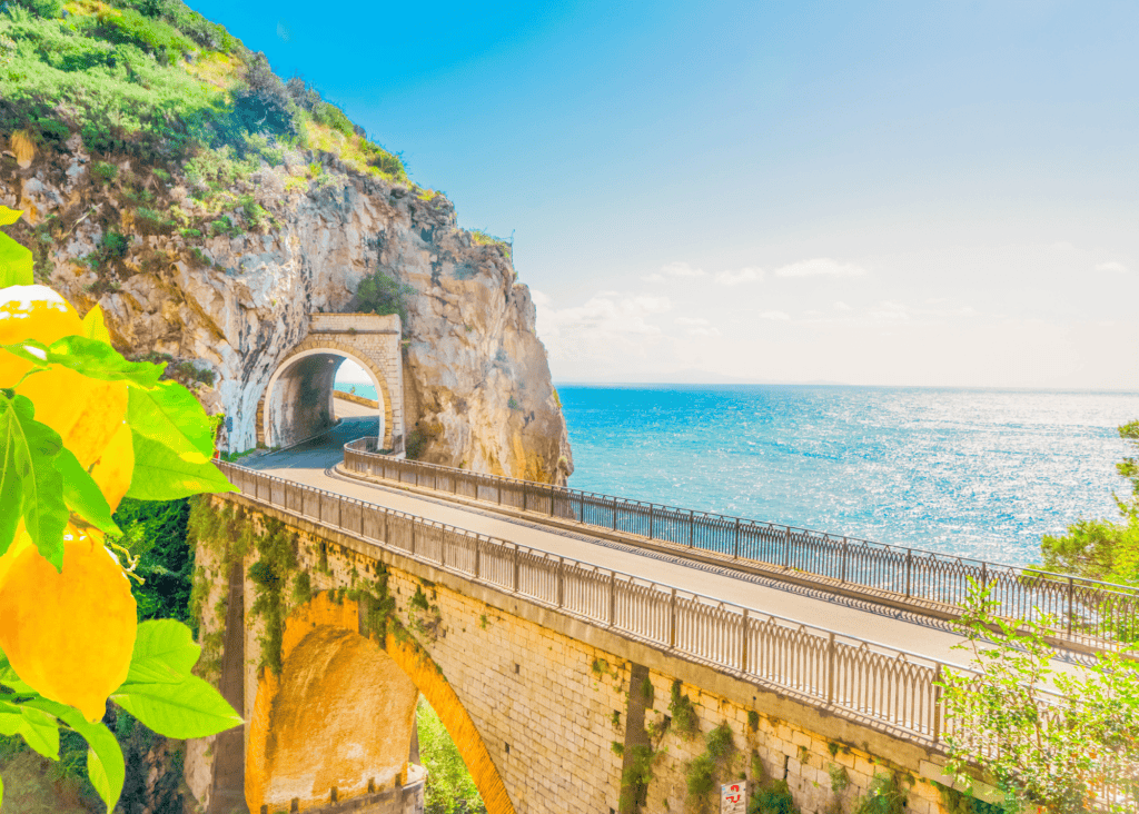Scenic coastal road and stone bridge along the Amalfi Coast Italy with turquoise sea and lemon trees in the foreground