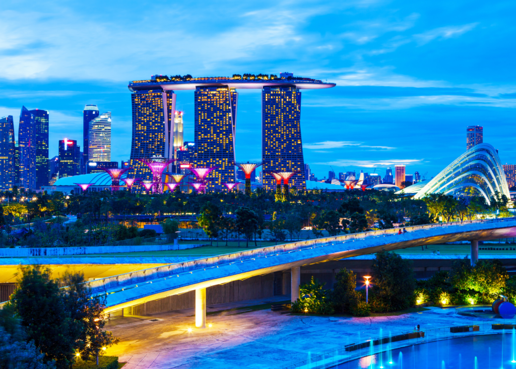 Singapore skyline at dusk with Marina Bay Sands hotel and illuminated Supertrees at Gardens by the Bay glowing against a blue evening sky.