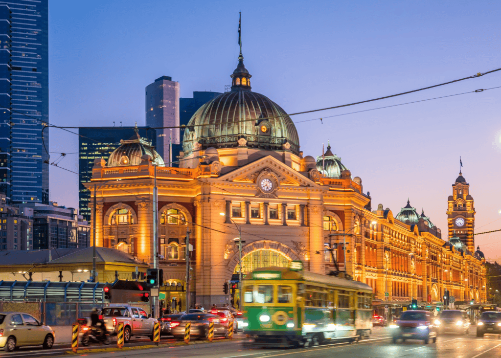 Flinders Street Station lit up at dusk with iconic green tram passing in front in Melbourne Australia