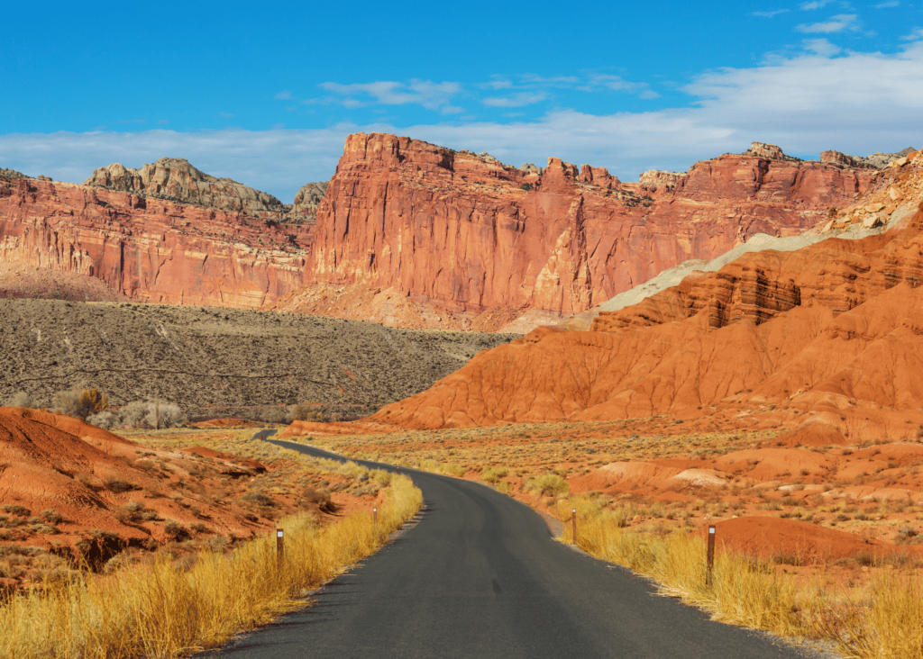 Empty paved road leading toward towering red and orange sandstone cliffs on the Capitol Reef National Park scenic drive in Utah.