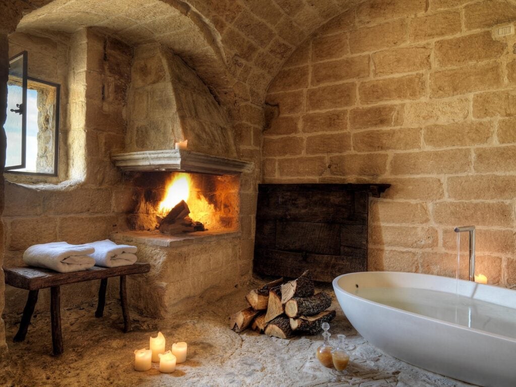Stone bathroom with fireplace and soaking tub inside a cave suite at Sextantio Le Grotte della Civita in Matera
