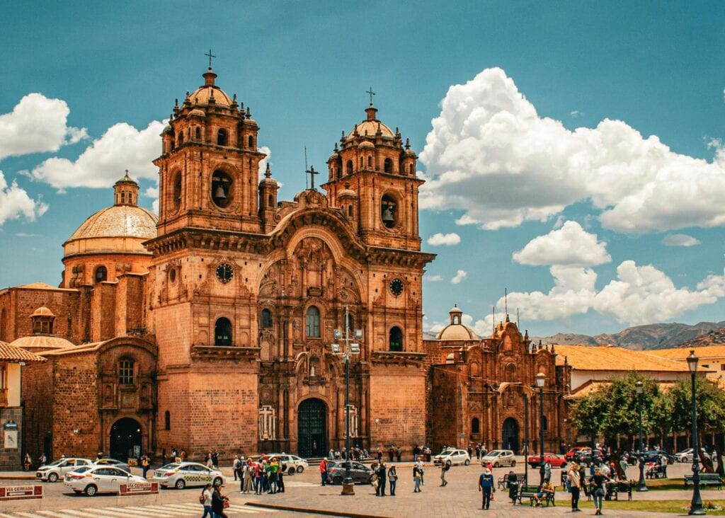 Ornate Spanish colonial cathedral with twin towers on the Plaza de Armas in Cusco Peru with locals and visitors in the foreground under a blue sky