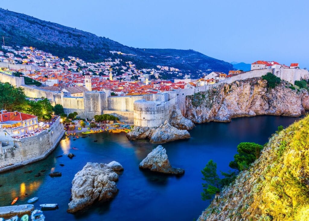 Aerial view of Dubrovnik's medieval city walls and harbor at dusk with terracotta rooftops glowing under a deep blue sky in Croatia