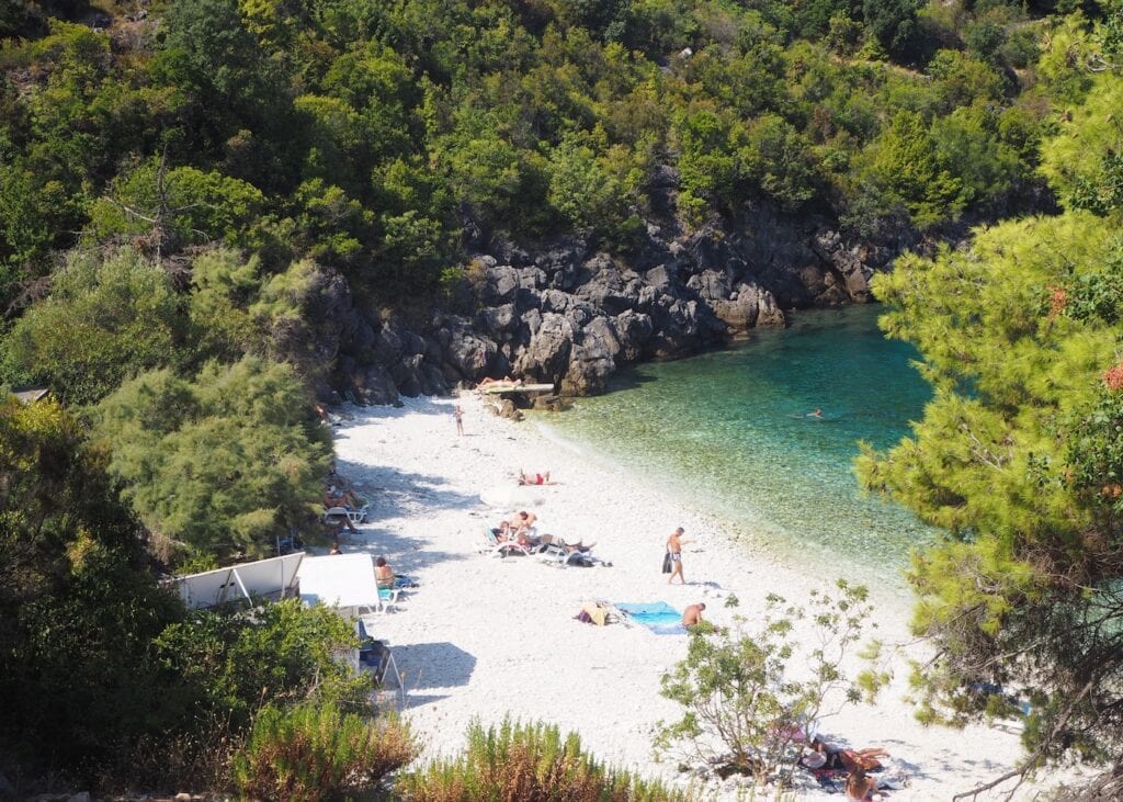 Small secluded pebble beach on Korčula Island in Croatia tucked between rocky cliffs and pine trees with clear turquoise water and sunbathers relaxing on the shore