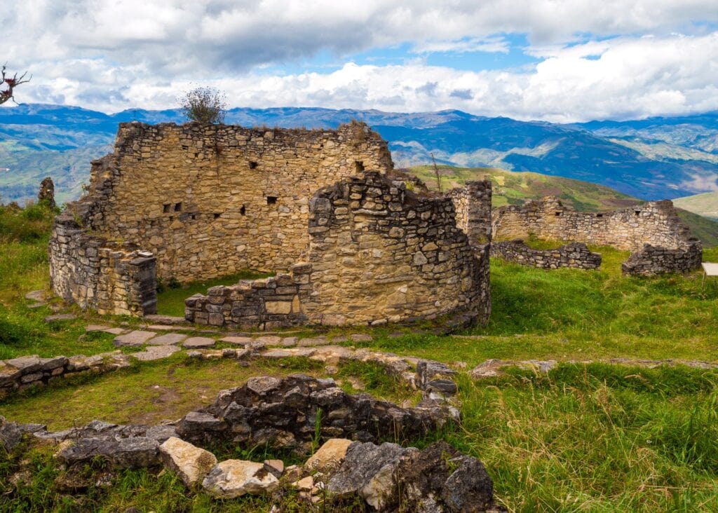 Ancient stone circular ruins of the Kuelap fortress city in the cloud forests of northern Peru with green hillsides and mountain ridges stretching into the distance