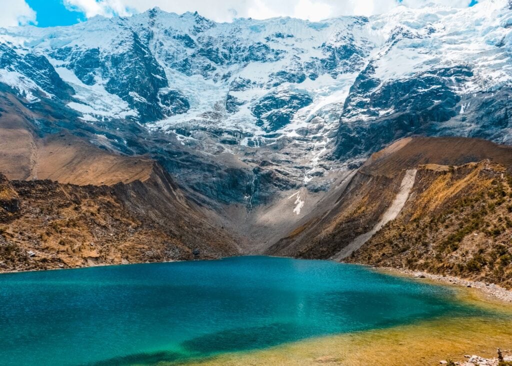 Vivid turquoise glacial water of Laguna Humantay Peru cradled by steep rocky slopes and snow-capped Andean peaks under a partly cloudy sky