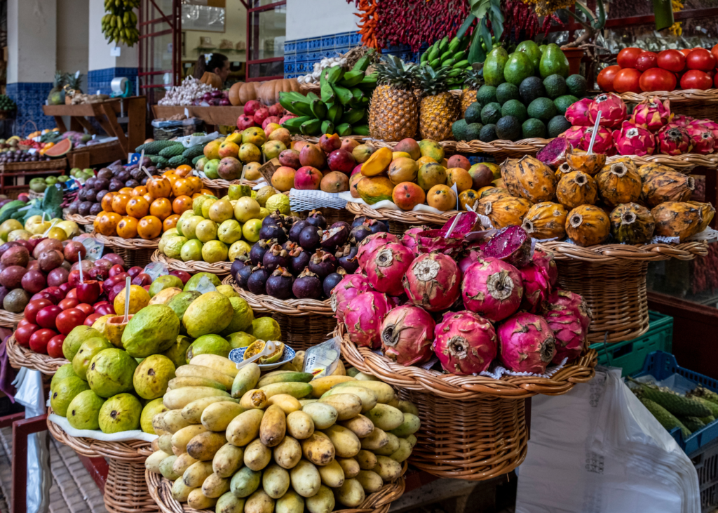 Colorful display of exotic tropical fruits including dragon fruit, bananas, and passion fruit piled high in wicker baskets at the Mercado dos Lavradores market in Funchal Madeira Portugal.