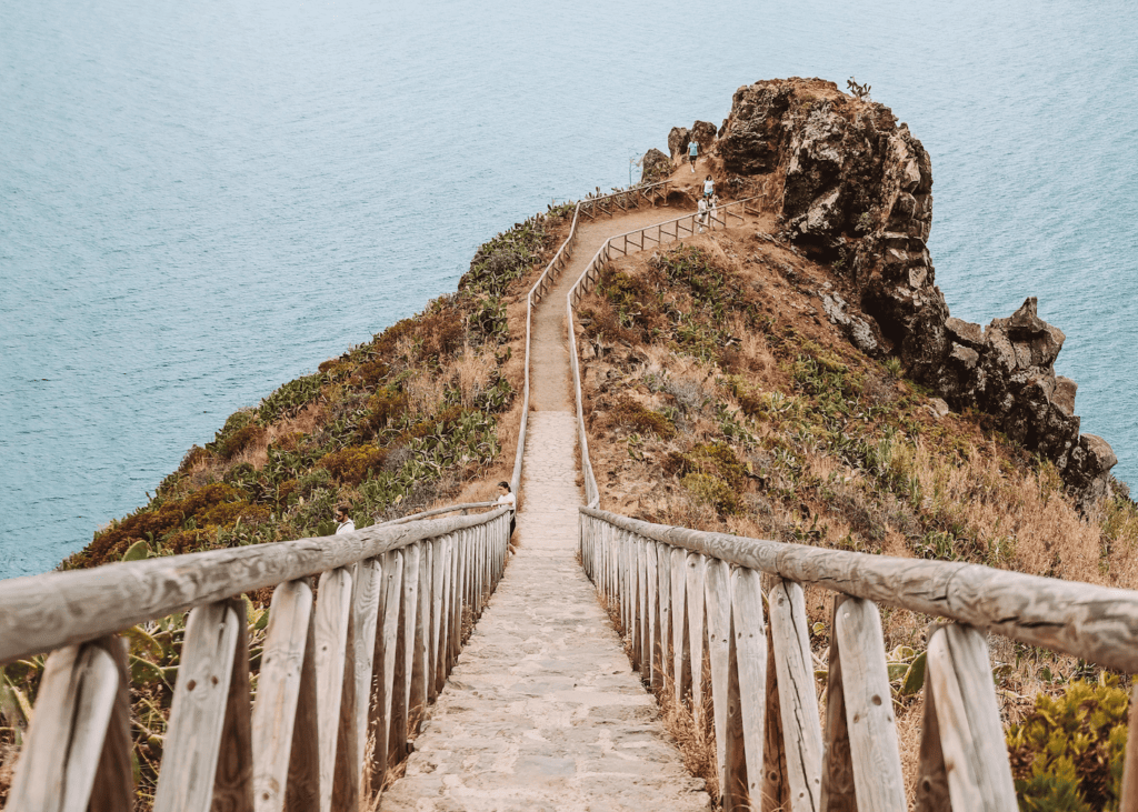 Narrow stone staircase with wooden railings leading out to a dramatic rocky volcanic headland surrounded by the blue Atlantic Ocean at Ponta de São Lourenço Madeira Portugal.