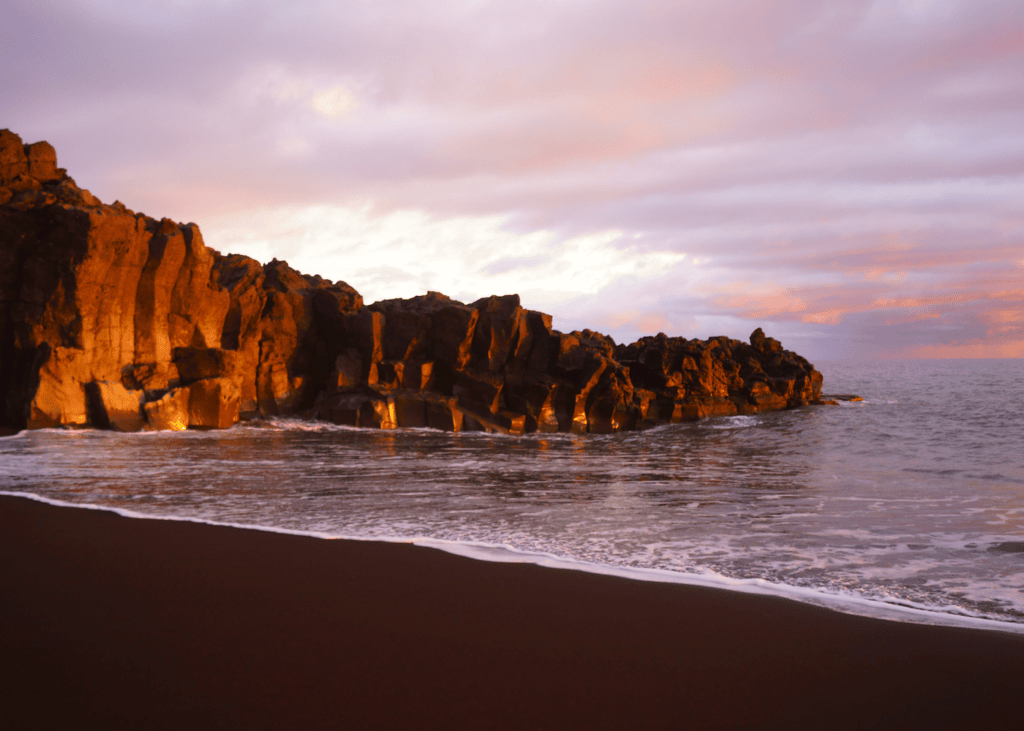 Two dramatic volcanic rock sea stacks silhouetted against a golden sunset sky with Atlantic waves crashing on the dark pebble beach at Ribeira da Janela Madeira Portugal.
