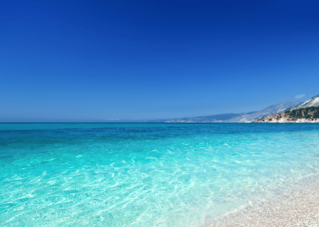 Brilliant turquoise and blue water stretches along the shoreline at Myrtos Beach in Kefalonia Greece with dramatic white limestone cliffs rising along the rugged coastline.