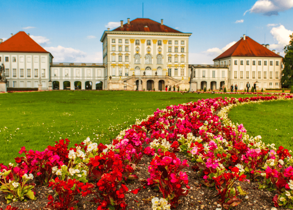 Nymphenburg Palace in Munich Germany viewed across colorful red and pink flower gardens on a sunny day.