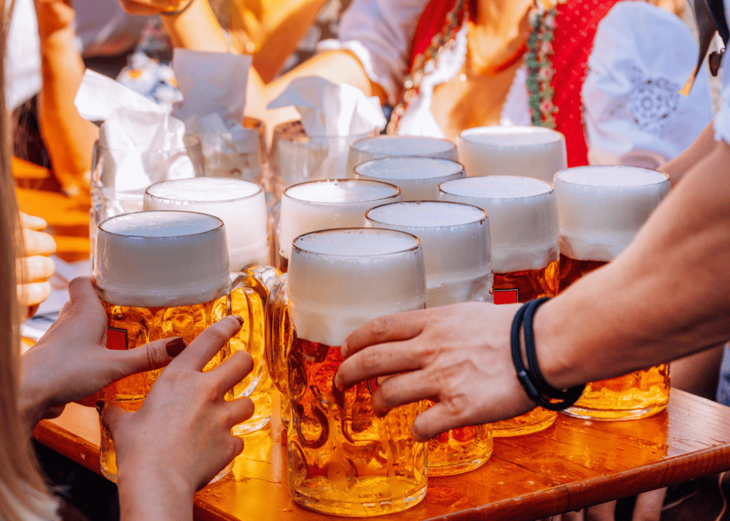 Multiple full beer steins being passed around a crowded table at Oktoberfest in Munich Germany.