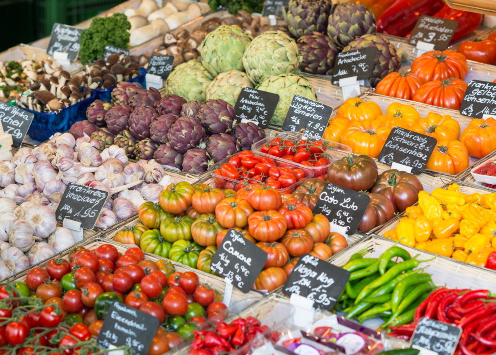 Colorful produce stall at Viktualienmarkt in Munich Germany with artichokes heirloom tomatoes garlic and fresh vegetables.