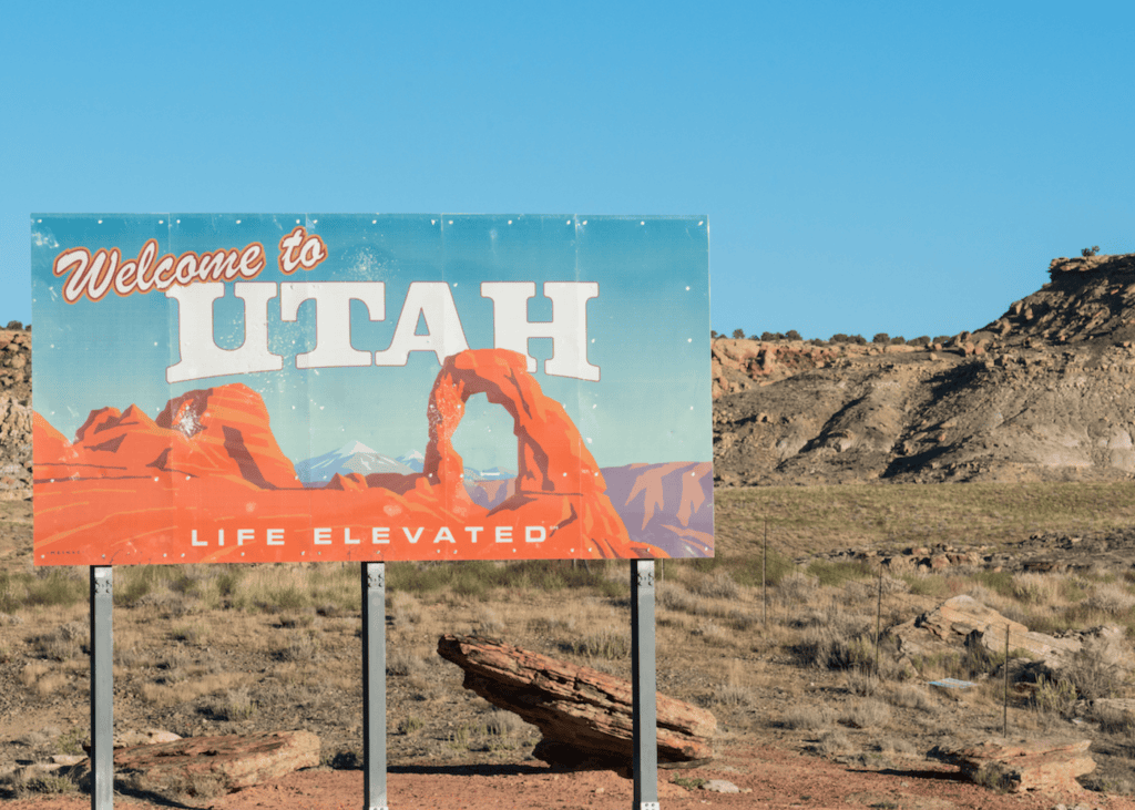 Welcome to Utah Life Elevated road sign surrounded by red rock desert landscape under a clear blue sky.