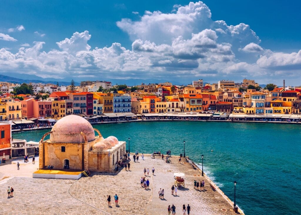 Aerial view of the old Venetian harbor in Chania, Crete with the Ottoman mosque, colorful waterfront buildings, and turquoise water