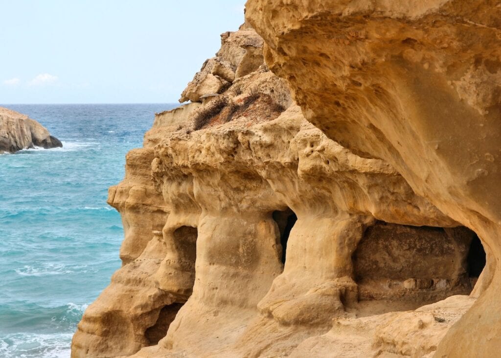 Ancient sandstone cave openings carved into the dramatic cliffs above the sea at Matala, Crete