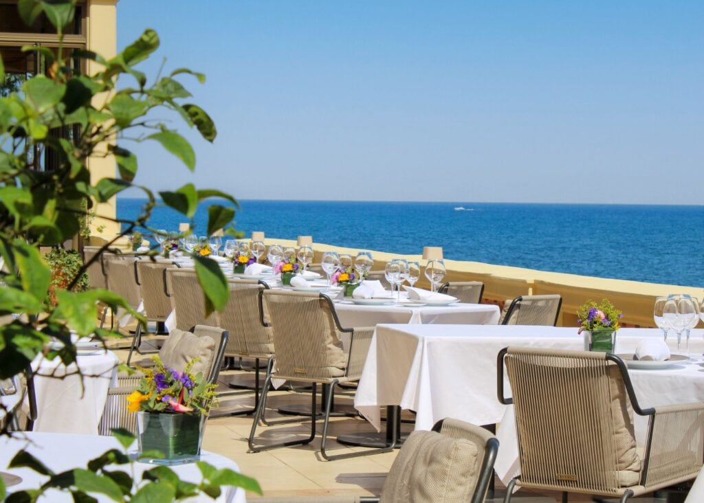Outdoor dining terrace at Royal Riviera hotel with white-clothed tables set with wine glasses and fresh flowers overlooking the open Mediterranean Sea
