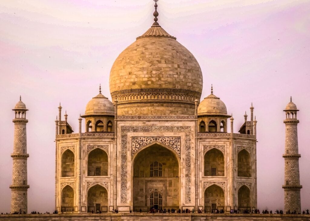 The Taj Mahal glowing in soft pink and gold light at sunrise in Agra, India.