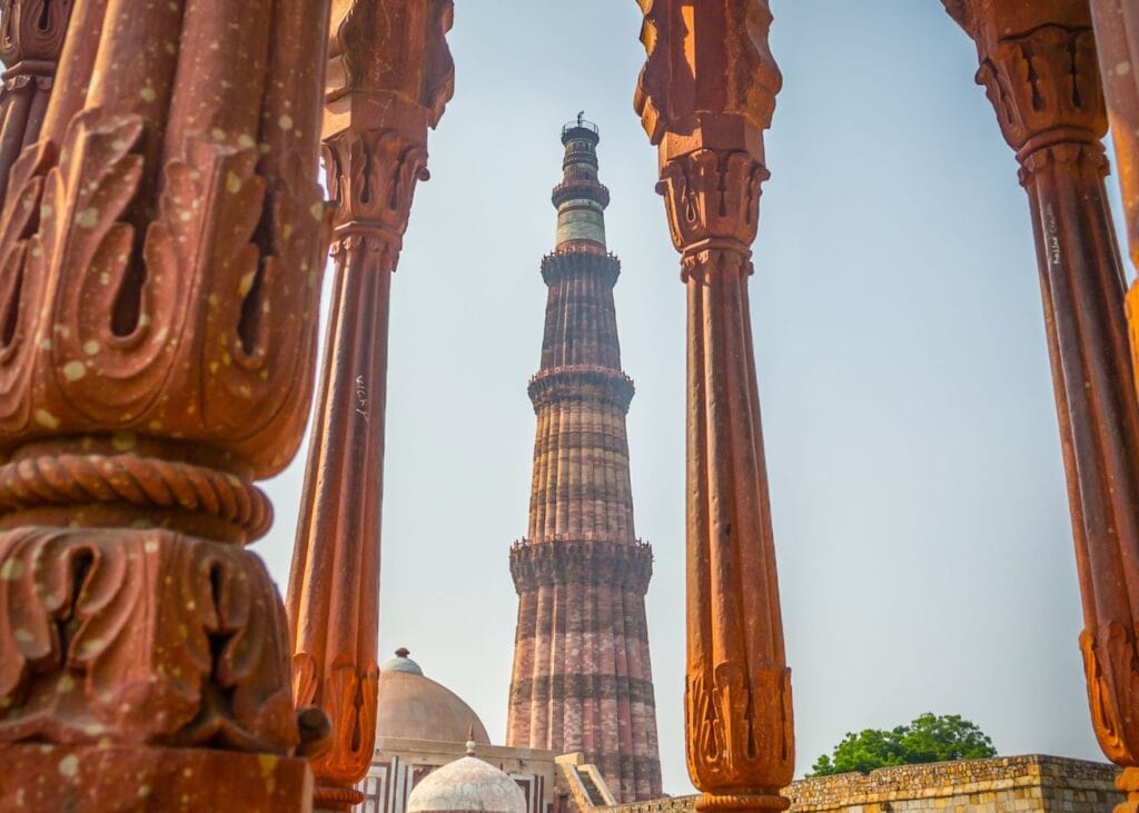 Qutub Minar tower in Delhi viewed through carved red sandstone pillars.