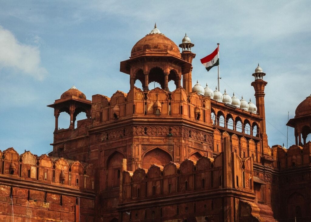 Red sandstone towers and domes of the Red Fort in Delhi with the Indian flag flying overhead.