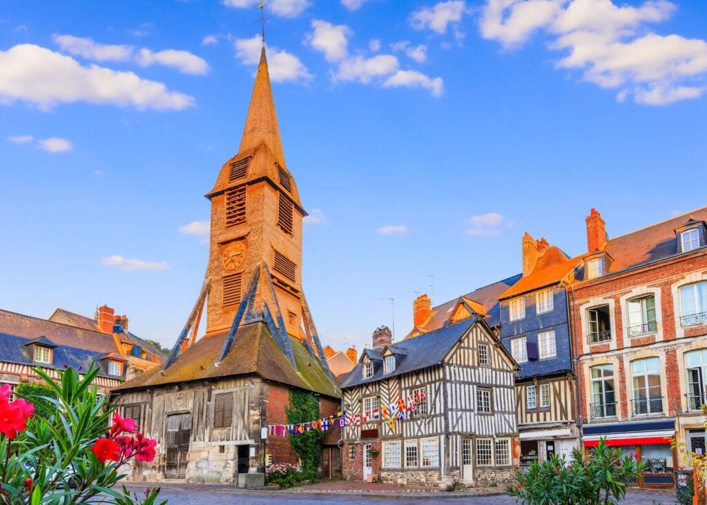 The main square in Honfleur Normandy with the distinctive wooden bell tower of Sainte-Catherine church and colorful half-timbered buildings decorated with bunting