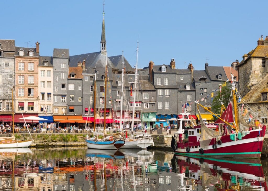 The Vieux Bassin harbor in Honfleur Normandy with colorful fishing boats and sailboats moored in front of the tall slate-fronted houses lining the quay