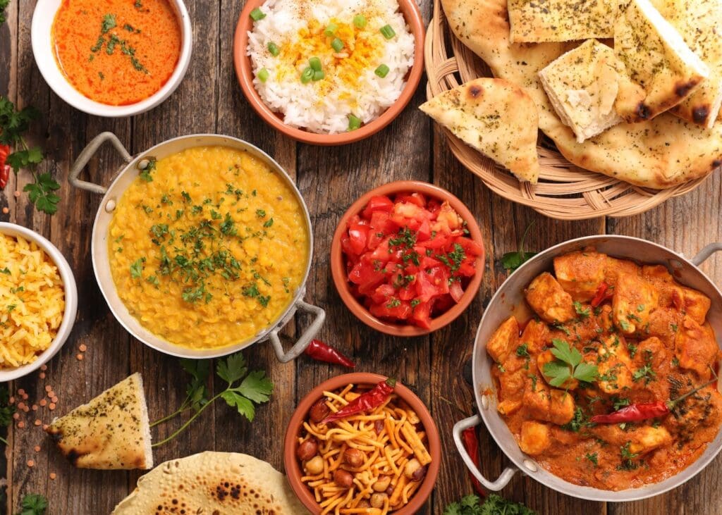 Spread of Indian dishes including curry, dal, naan, rice, and chutneys on a wooden table.