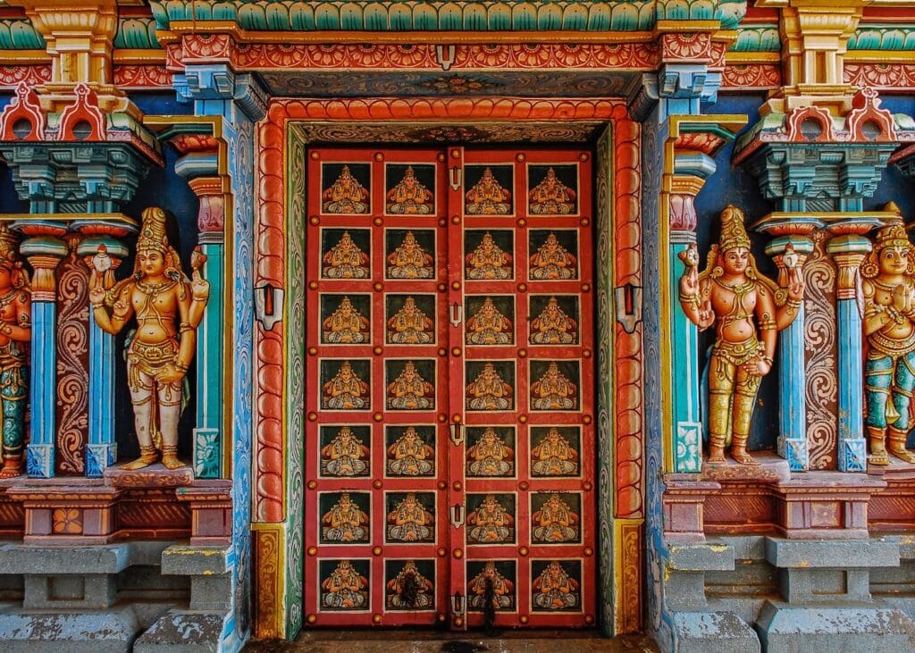 Ornate Hindu temple entrance with a red carved door and colorful painted deity statues.