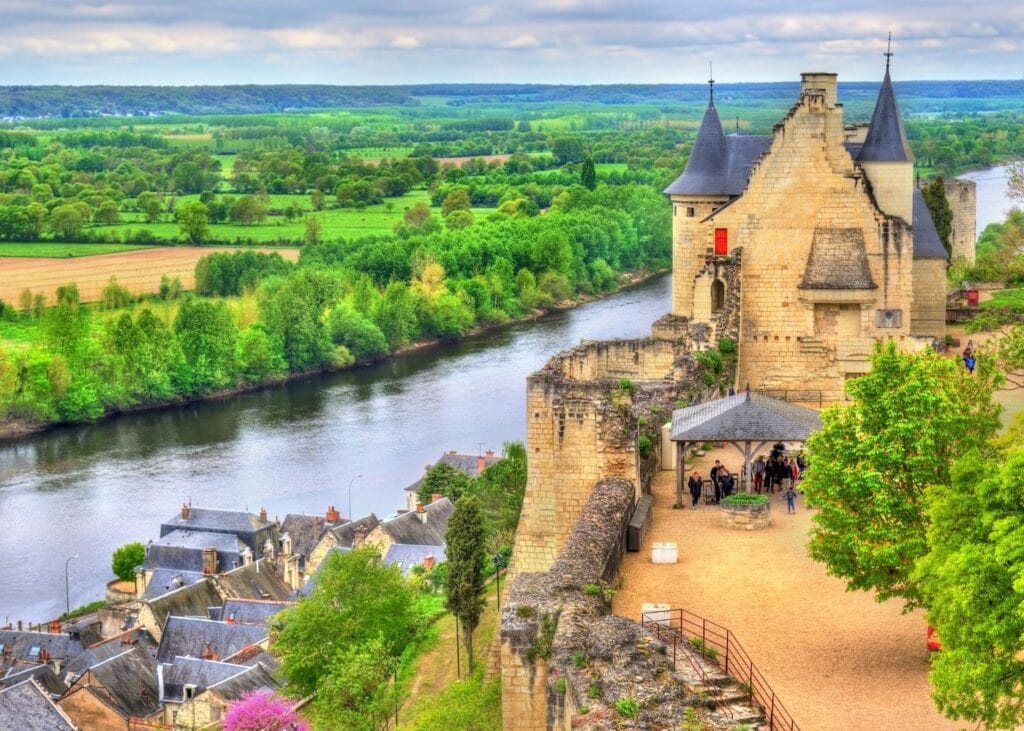 A medieval château perched above the Loire River with the valley town below and rolling green countryside stretching to the horizon